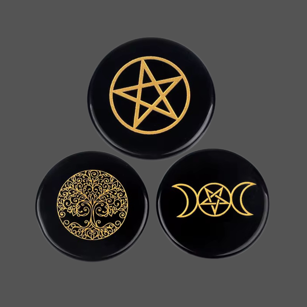 Three round black obsidian stones featuring carved occult and mystical designs, including a pentagram, a tree of life, and triple moon phases, arranged on a dark gray background.