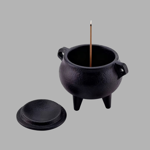 A black cast-iron incense burner with a lid placed beside it, shown on a plain gray background. A single incense stick stands upright inside the pot.