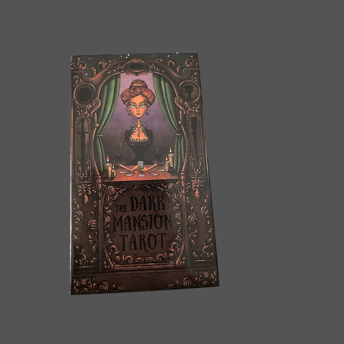 Dark Mansion Tarot deck box, featuring an ornate dark brown gothic illustration of a woman at a card table with green curtains.