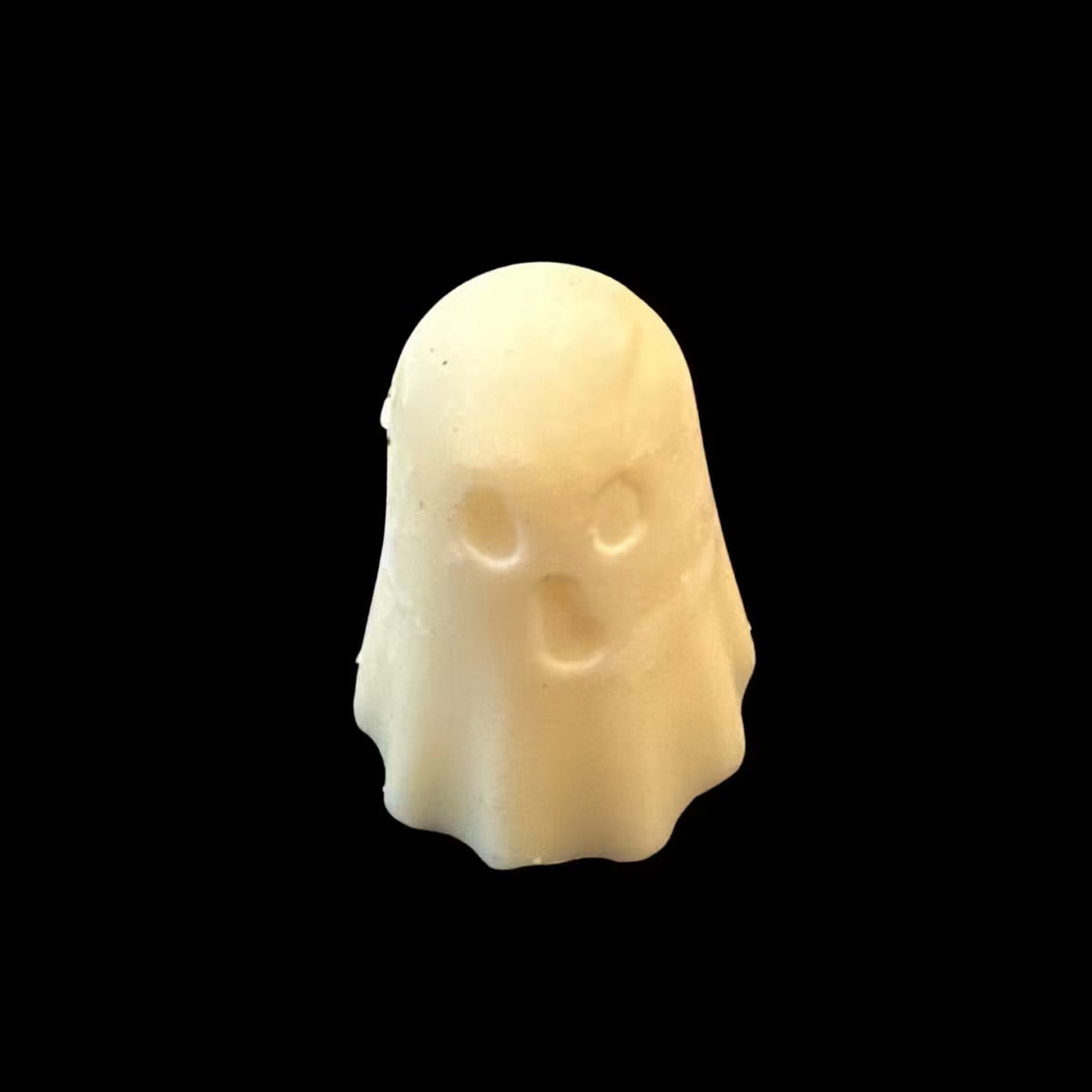 A small cream-colored ghost-shaped soy wax melt with simple facial cutouts, centered against a solid black background.