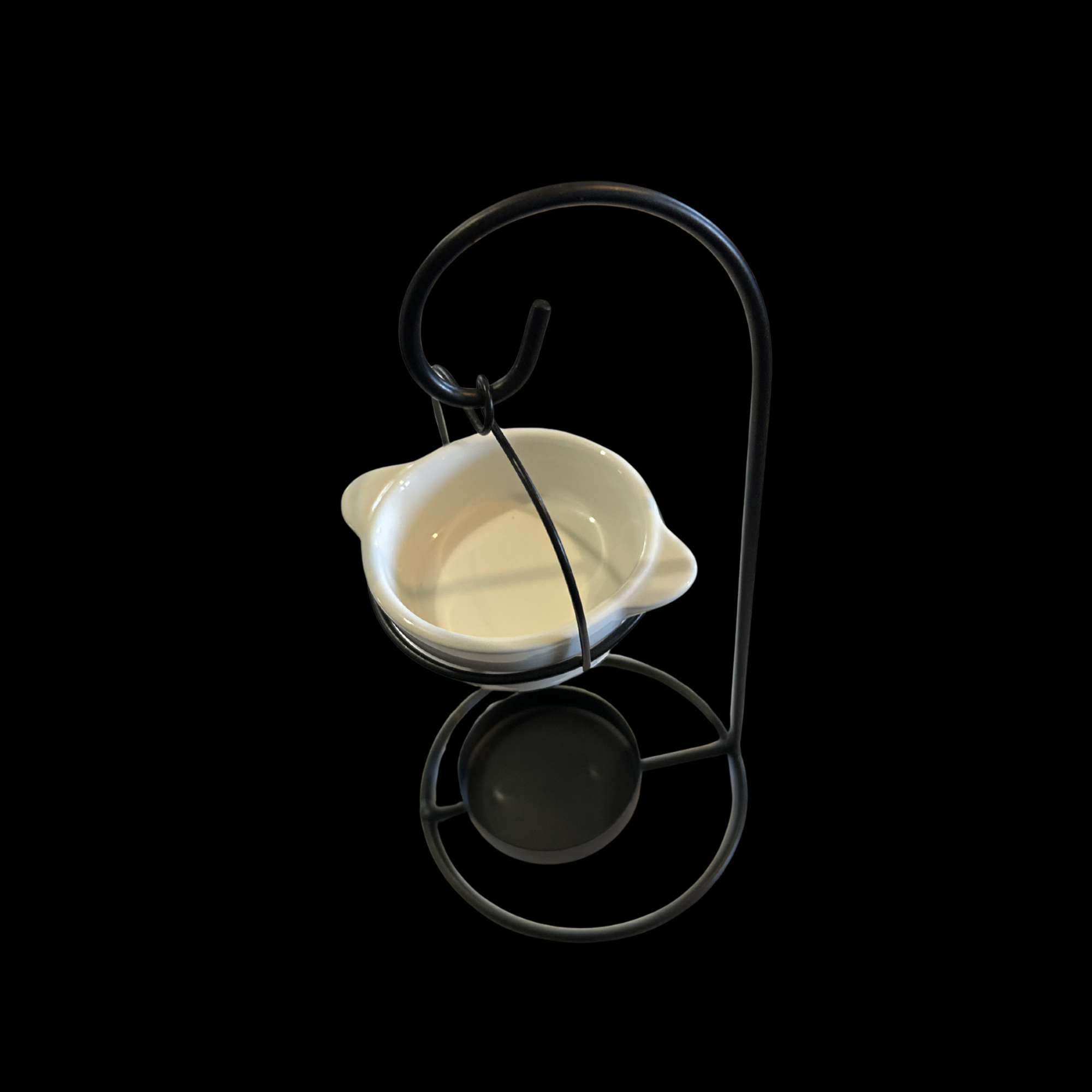 A white ceramic candle holder with small side tabs, suspended in a black metal stand with a circular base with tea light holder, curved top loop, shown against a solid black background 