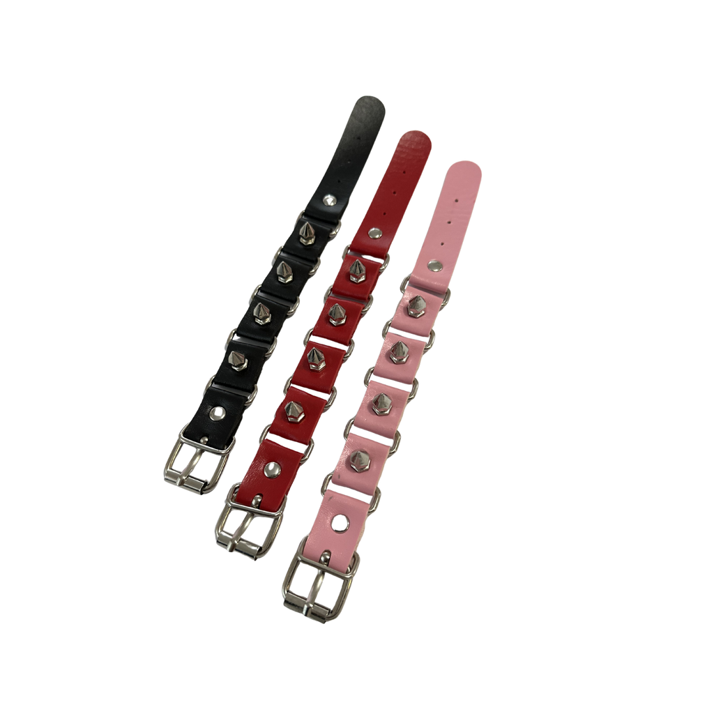 3 spike wrist cuffs laying flat next to each other, black, red and pink